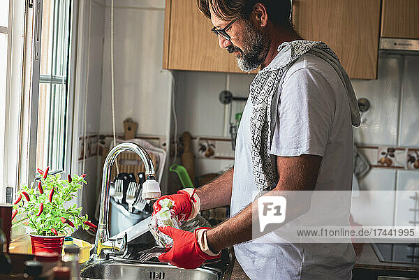 Mature man cleaning glass in kitchen