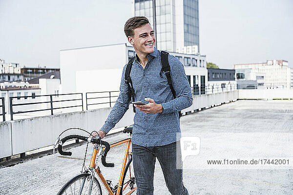 Young man with bicycle walking on parking garage rooftop