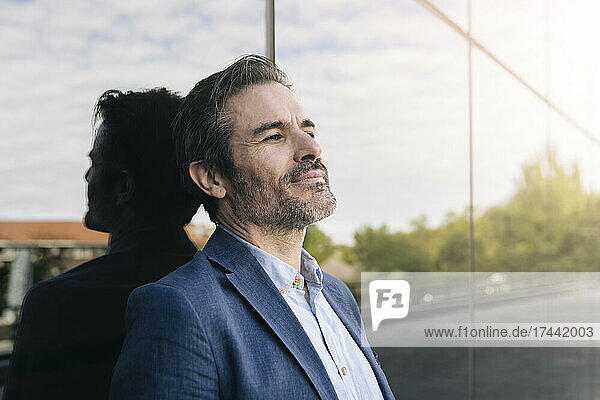 Mature businessman contemplating while leaning on glass