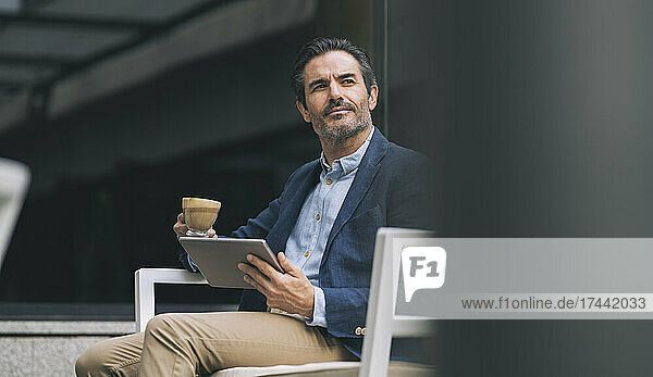 Mature male professional holding digital tablet and coffee cup while sitting on chair