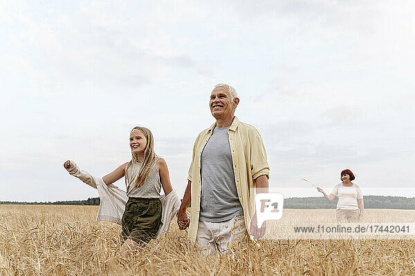 Enkelin hält Großvater beim Gehen auf dem Feld an den Händen