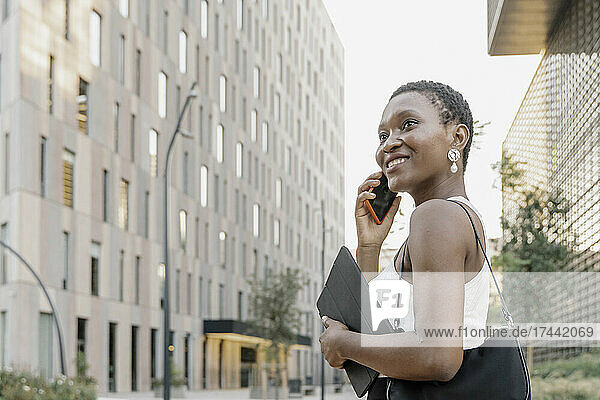 Smiling businesswoman with digital tablet talking on mobile phone in city