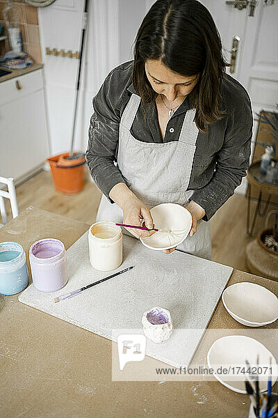 Young craftswoman painting bowl at workbench