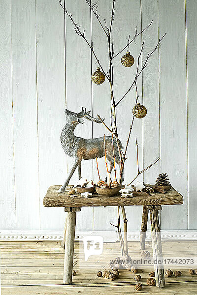 Bare twigs decorated with Christmas ornaments and wooden stool with deer figurine  walnuts and Christmas cookies