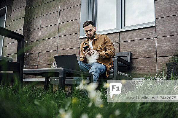 Male freelancer working on mobile phone in backyard