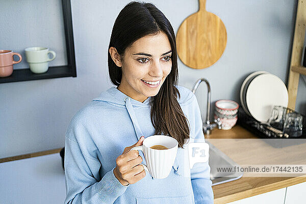 Beautiful young woman holding coffee mug in kitchen at home