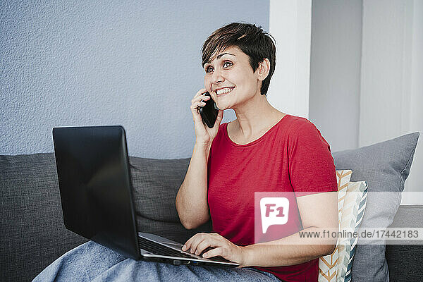 Excited businesswoman talking on smart phone while sitting with laptop at home