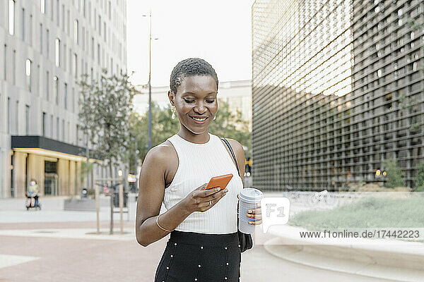 Businesswoman with disposable coffee cup using mobile phone in city