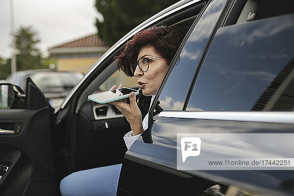 Mature businesswoman talking on smart phone through speaker while sitting in car
