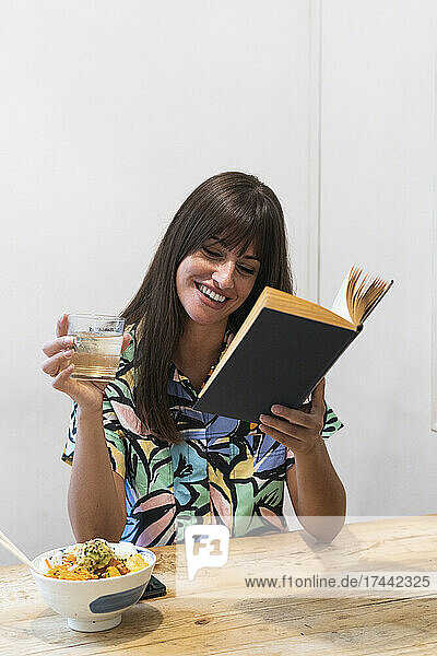 Lächelnde Frau liest Buch im Restaurant