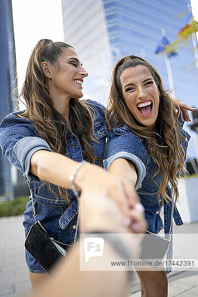 Happy female identical twin holding hand of friend