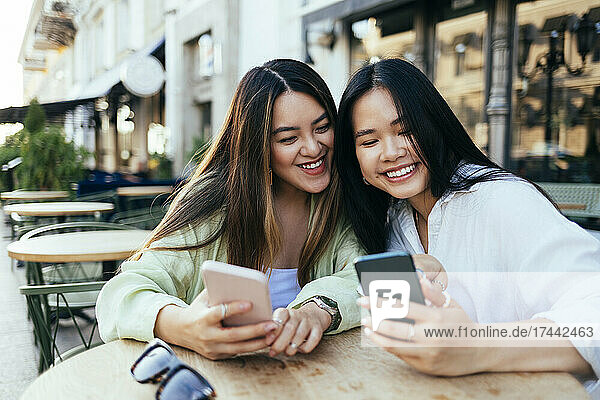 Glückliche Freundinnen  die Smartphones im Straßencafé nutzen