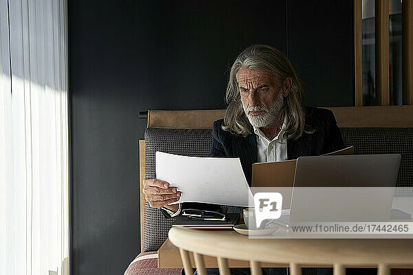 Männlicher Fachmann prüft Dokument  während er am Tisch im Hotelcafé sitzt