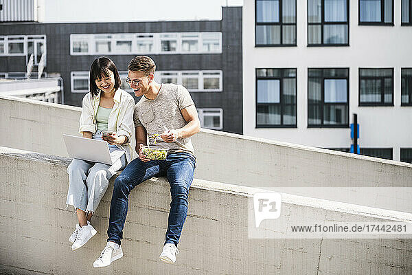 Happy male and female friends sharing laptop during sunny day