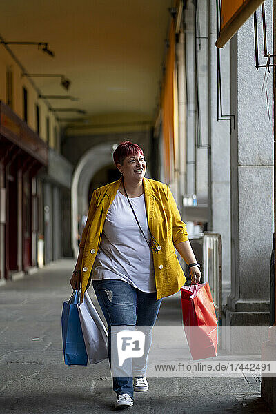 Lächelnde Frau mit Einkaufstüten  die am Flur läuft