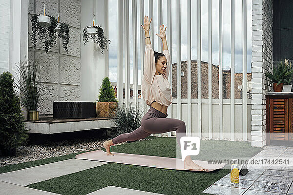 Woman with arms raised stretching leg while practicing yoga on terrace