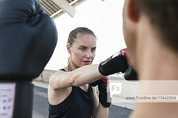 Concentrated female athlete practicing boxing with male coach