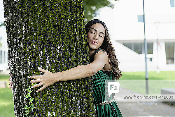 Beautiful woman with eyes closed hugging tree trunk