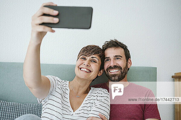 Smiling couple taking selfie through smart phone at home