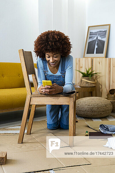 Woman using mobile phone while leaning on wooden chair