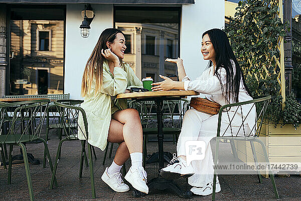 Smiling female friends talking at sidewalk cafe