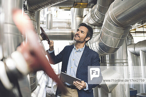 Businessman holding digital tablet while checking machinery at industry