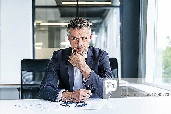 Businessman with hand on chin sitting at desk in office
