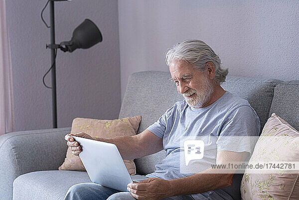 Älterer Mann benutzt Laptop  während er auf dem Sofa sitzt