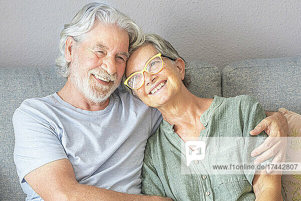 Lächelndes älteres Paar sitzt auf dem Sofa im Wohnzimmer
