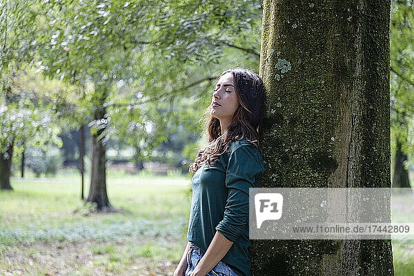Beautiful woman with eyes closed leaning on tree trunk