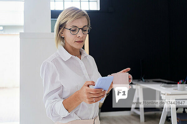 Businesswoman with coffee mug using smart phone in office