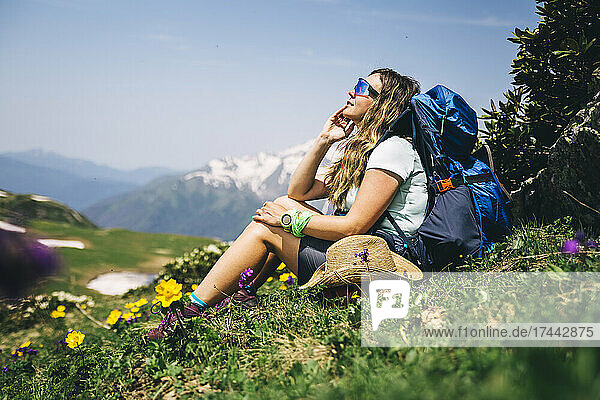 Wanderin mit Sonnenbrille und Rucksack sitzt auf Gras