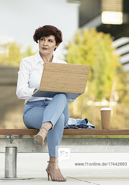 Beautiful businesswoman sitting with laptop on bench at office park