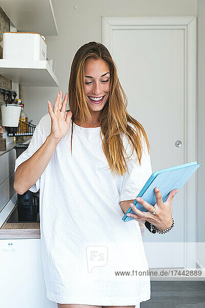 Woman waving during video call through digital tablet at home
