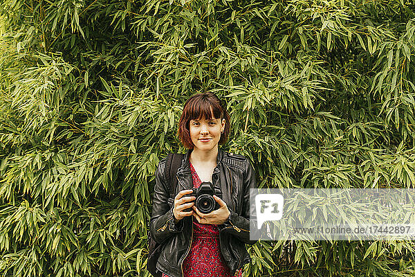 Female photographer with bangs holding camera in front of plants