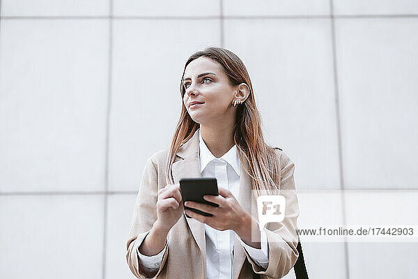 Businesswoman holding smart phone in front of wall