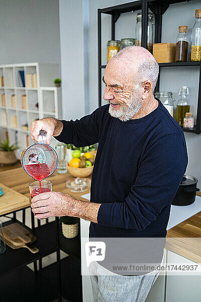 Senior man pouring smoothie in drinking glass at home