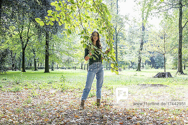 Woman holding branches while standing at park