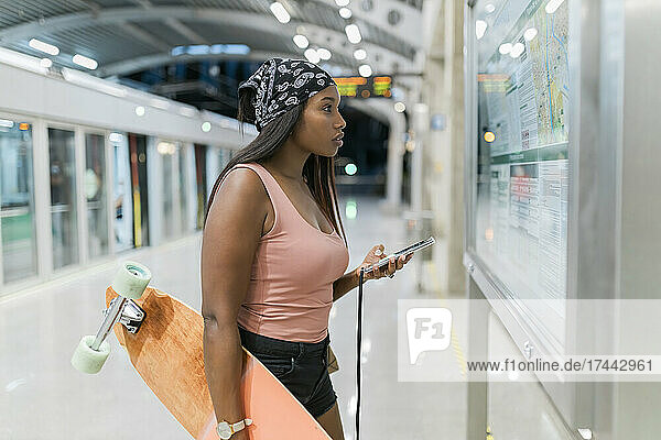 Woman with skateboard and mobile phone checking map at station