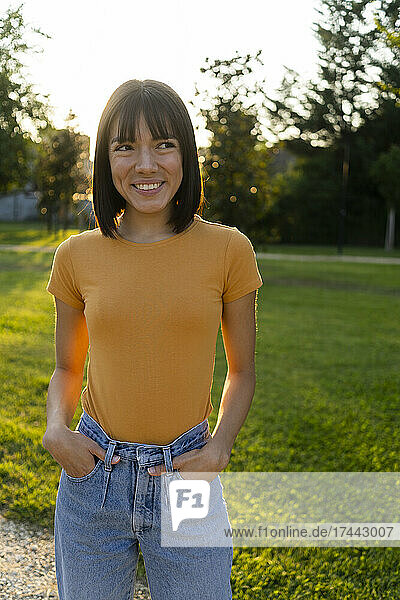 Smiling woman with hands in pockets standing at lawn