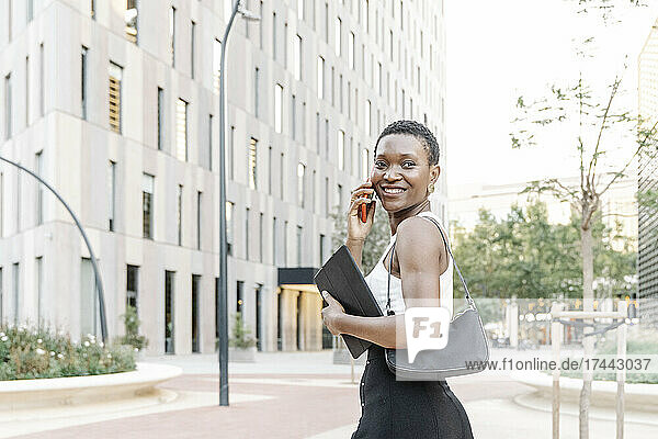 Happy female business professional talking on mobile phone while walking in city