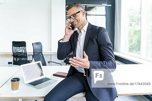 Smiling businessman gesturing while talking on mobile phone in office
