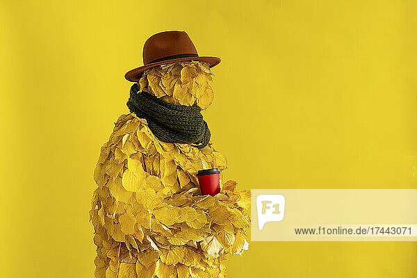 Woman wearing hat and leaf costume holding disposable cup by yellow background