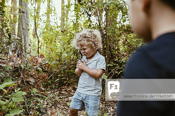 Boy with male friend looking at plant through magnifying glass