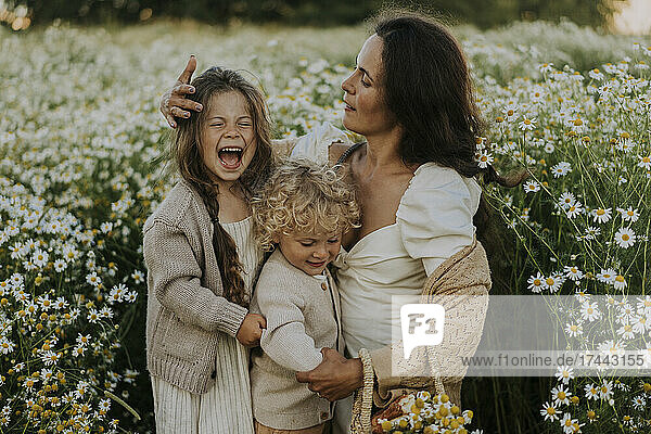 Mother with cheerful daughter and son amidst flowering plants on field