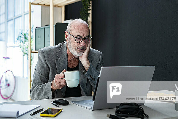 Businessman with coffee cup looking at laptop in studio