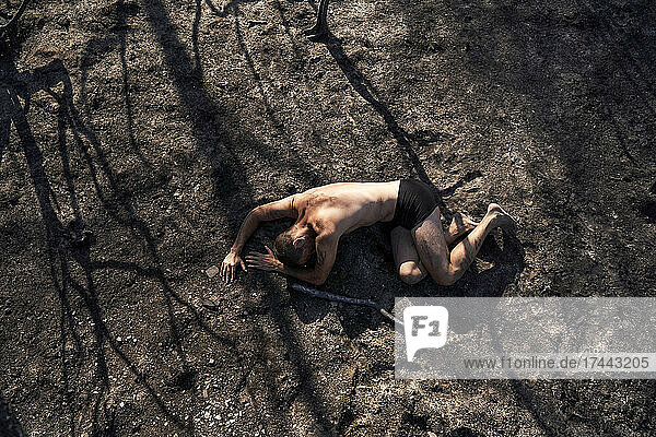 Lonely man lying on burned forest floor