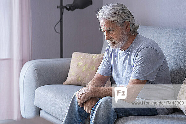 Lonely senior man sitting on sofa at home