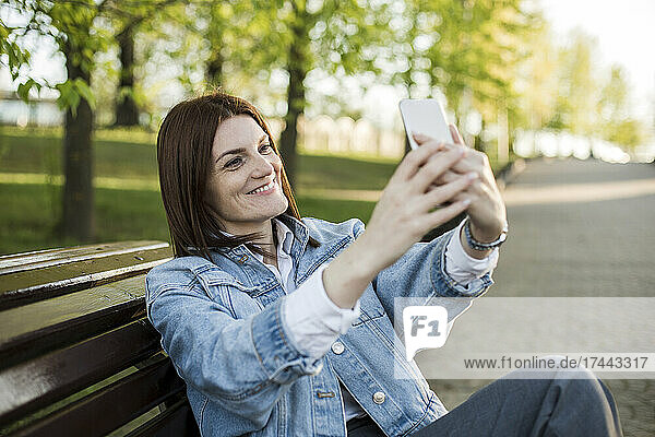 Smiling woman taking selfie through mobile phone on bench