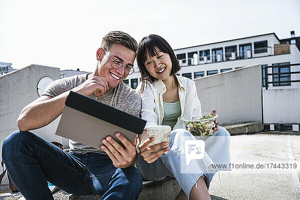 Male and female friends sharing digital tablet and smart phone during sunny day